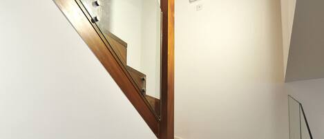 Un escalier en bois avec des rampes en verre, des murs blancs et un plafond avec des poutres en bois.