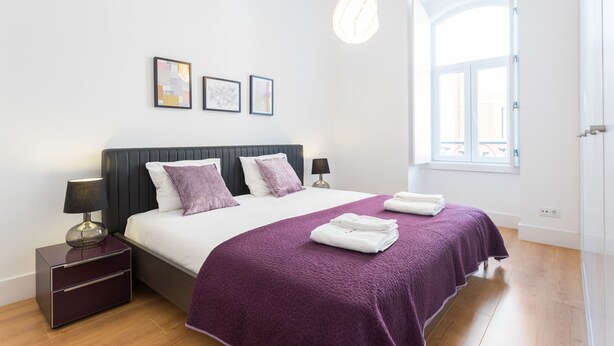 Een moderne slaapkamer met een groot bed, een nachtkastje, een lamp en een raam met uitzicht.