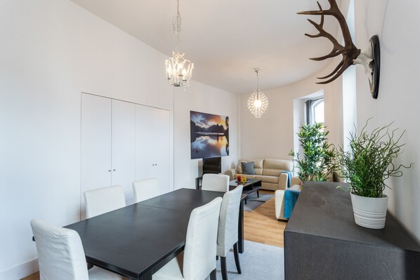 A modern living room with a dining area, a large flat-screen TV, a chandelier, and a mounted deer head.