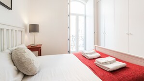 Een hotelkamer met een bed, nachtkastje, lamp, rode handdoek op de vloer en een kledingkast.