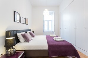 A bedroom with a bed, a nightstand, a lamp, a window, and a wardrobe.