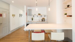 Una cocina moderna con armarios blancos, una isla central, iluminación colgante y un comedor con sillas blancas.