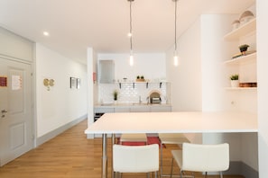 A modern kitchen with white cabinetry, a central island, pendant lighting, and a dining area with white chairs.
