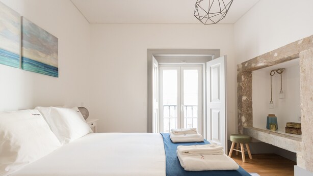 Un dormitorio con una cama grande, un muro azul decorativo, un taburete de madera y una pared de piedra rústica.