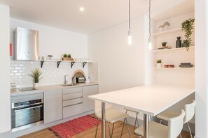 A modern kitchen with white cabinetry, a built-in oven, and a white dining table with bar stools.