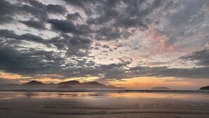 A beach with a sunset, mountains in the background, and a calm sea. - Recanto Soga Chalés (Ubatuba)