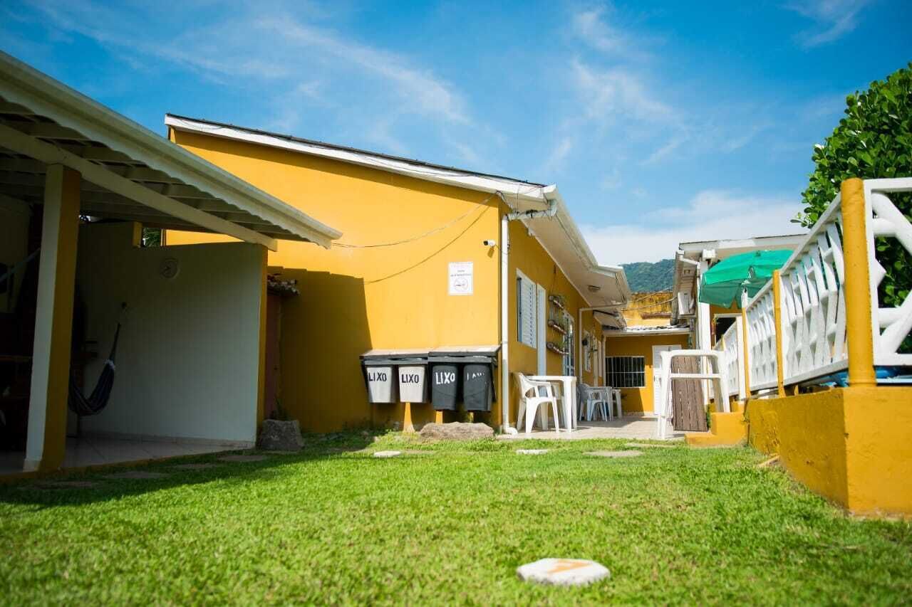 Um edifício amarelo com um alpendre coberto, área de estar ao ar livre e latões de lixo identificados com 'LIXO'.