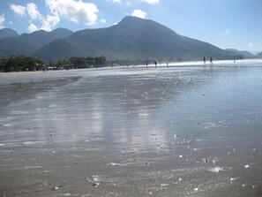 A beach with mountains in the background, sandy shore, and people walking. - Recanto Soga Chalés (Ubatuba)