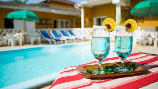 Two glasses of blue liquid with garnishes on a wooden tray by a poolside. - Recanto Soga Chalés (Ubatuba)