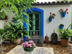 A courtyard with a blue door, potted plants, a metal chair, and a tiled floor.