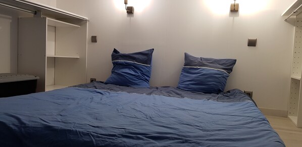 Un dormitorio con una cama, dos almohadas, un armario y una mesita de noche.