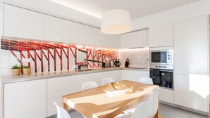 Une cuisine moderne avec des meubles blancs, une table à manger en bois et une structure métallique rouge originale qui orne le mur derrière l’évier.
