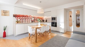 Une cuisine moderne avec des meubles blancs, une table à manger en bois et un mur d’accent rouge.
