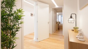 Un couloir moderne avec une plante en bambou, une porte blanche et un bureau agrémenté d’une lampe et d’une petite statue.