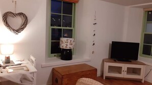 A living room with a desk, a television on a cabinet, a window with a heart-shaped decoration, and a wall-mounted bird feeder.