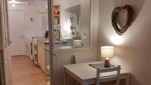 A compact kitchen with a dining area, a heart-shaped wall decoration, and a lamp on the table.