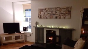 A living room with a fireplace, a television, and a window with blinds.