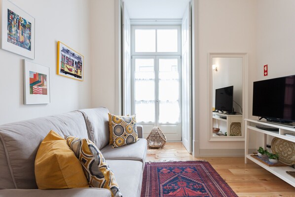 A living room with a grey sofa, a red and blue rug, and a television on a white stand.