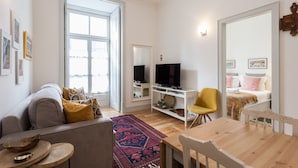 A modern living room with a sofa, a TV, a dining table, and a yellow chair. - FLH Bacalhoeiros Charming Place (Lisbon)