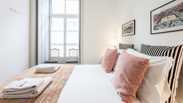 A hotel room with a bed, a window with a view, a lamp, and a painting on the wall. - FLH Bacalhoeiros Charming Place (Lisbon)