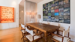 A dining area with a wooden table and chairs, a large abstract painting, and a collage of images on the wall. - FLH Chiado Design Flat (Lisbon)