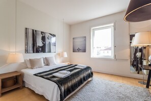 A modern bedroom with a large bed, two bedside tables, a window, and artwork on the walls.