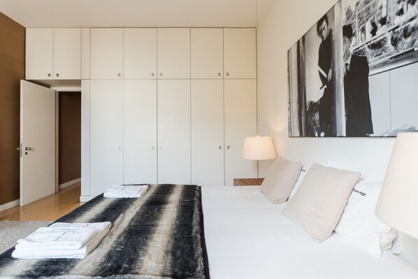 A hotel room with a bed, a large wardrobe, a painting on the wall, and a lamp.