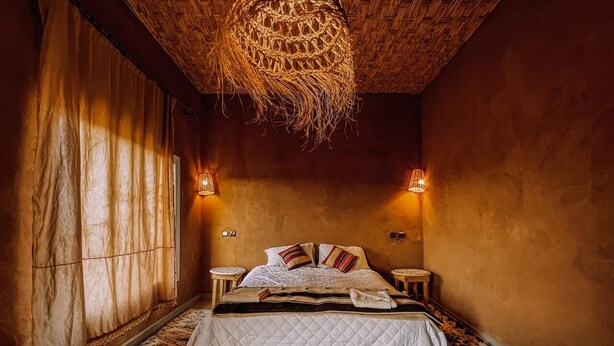 A cozy bedroom with a large bed, two bedside tables, a woven ceiling light, and a patterned rug. - Dar Talmoudi (Tagounite)