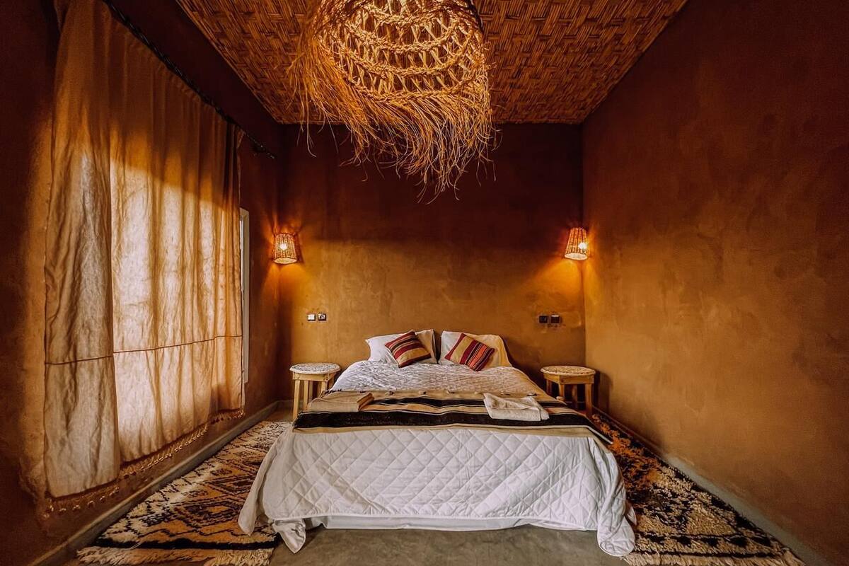 Um quarto aconchegante com uma cama grande, duas mesas de cabeceira, uma luminária de teto trançada e um tapete estampado.