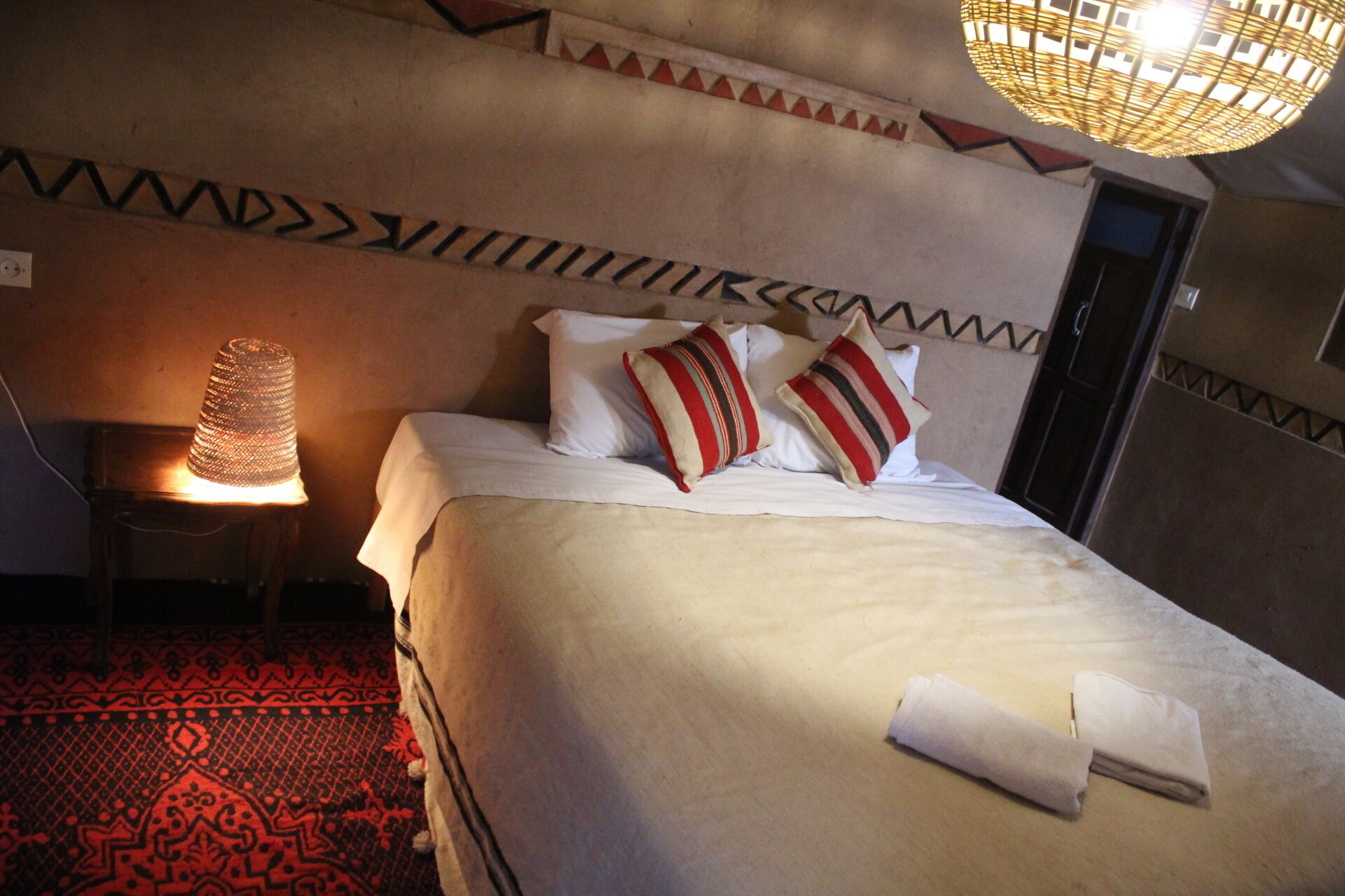 A hotel room with a bed, pillows, a nightstand, a lamp, and a patterned carpet.