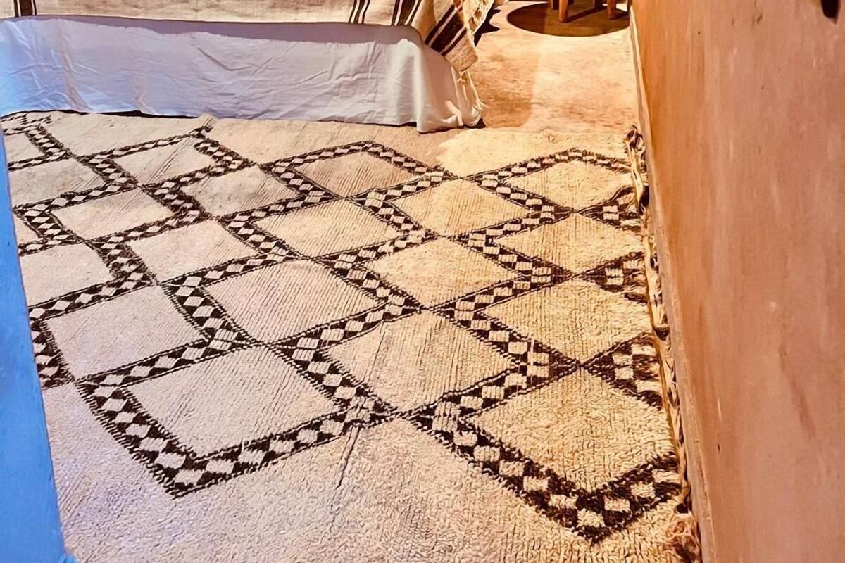 Quarto com cama, duas almofadas, uma mesinha redonda e luminária na parede.