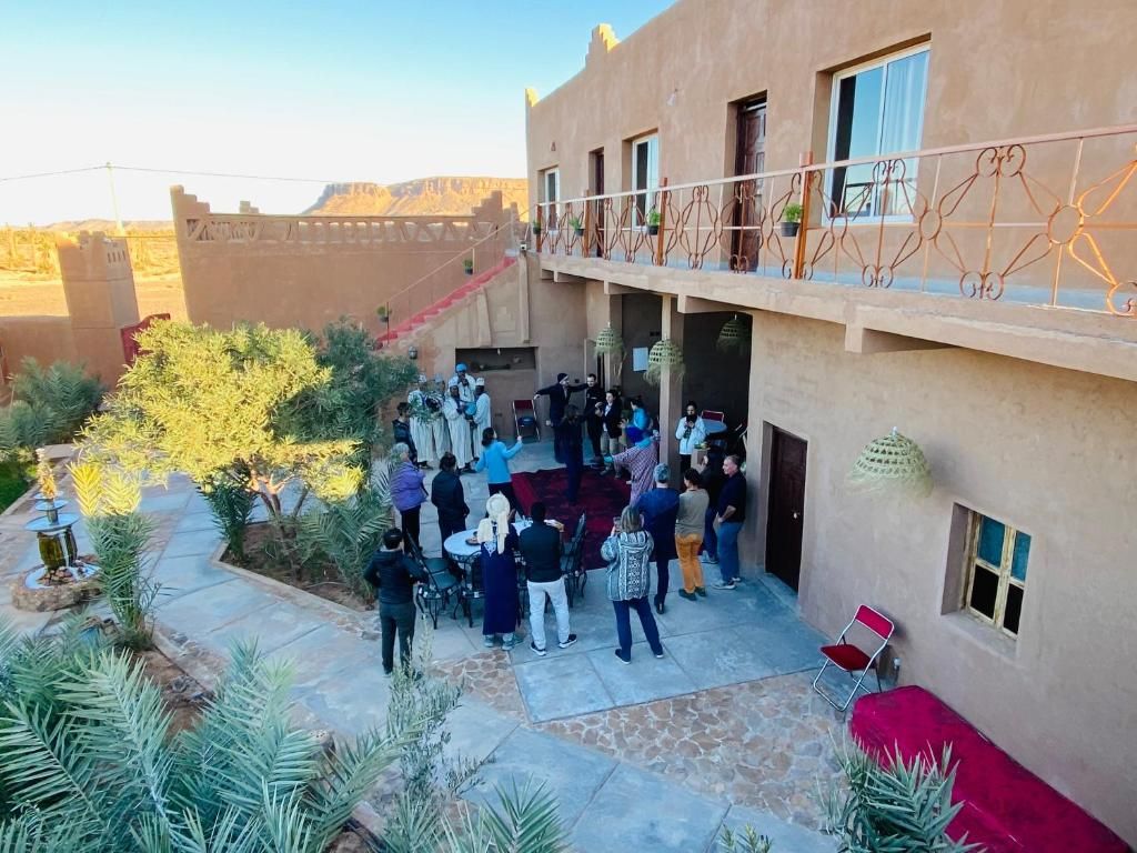 Um pátio com um grupo de pessoas reunidas em volta de uma mesa, um edifício com varanda e vista para a paisagem circundante.