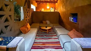 A cozy, rustic interior with a wooden ceiling, a striped rug, and a sofa with cushions. - Dar Talmoudi (Tagounite)