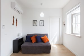 A modern living room with a grey sofa, two framed wall art pieces, a black side table, and a window with natural light.