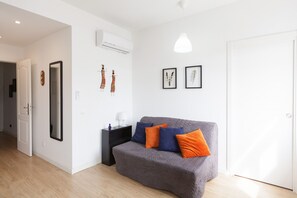 A modern living room with a grey sofa, two orange cushions, a black side table, and a white pendant light.