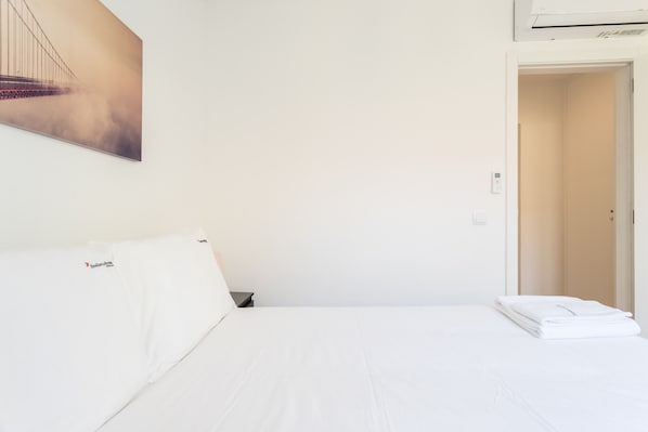 A hotel room with a bed, a nightstand, a folded white towel, and a painting of a bridge on the wall.