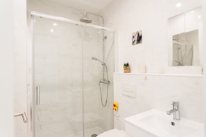 Ein modernes Badezimmer mit einer gläsernen Dusche, einem weißen Waschbecken und einem Spiegel darüber.