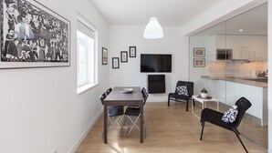 Ett modernt kök med en stor TV, en matplats med bord och stolar samt ett vardagsrum med soffa och fåtöljer.