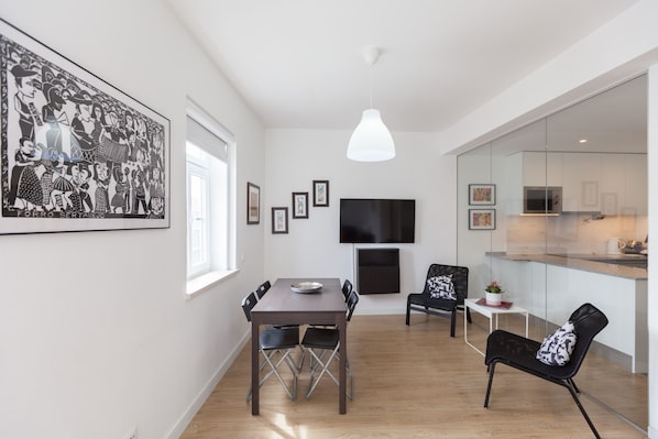 A modern kitchen with a large TV, a dining area with a table and chairs, and a living area with a sofa and chairs.