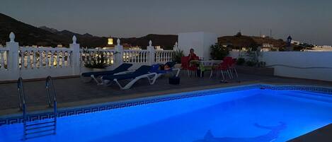 Una piscina en la azotea con diseño de delfín, sillones de descanso y un área de comedor con mesas y sillas.