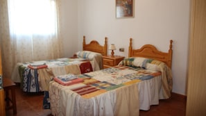 Quarto com duas camas de solteiro, mesa de cabeceira, abajur e janela com cortinas.