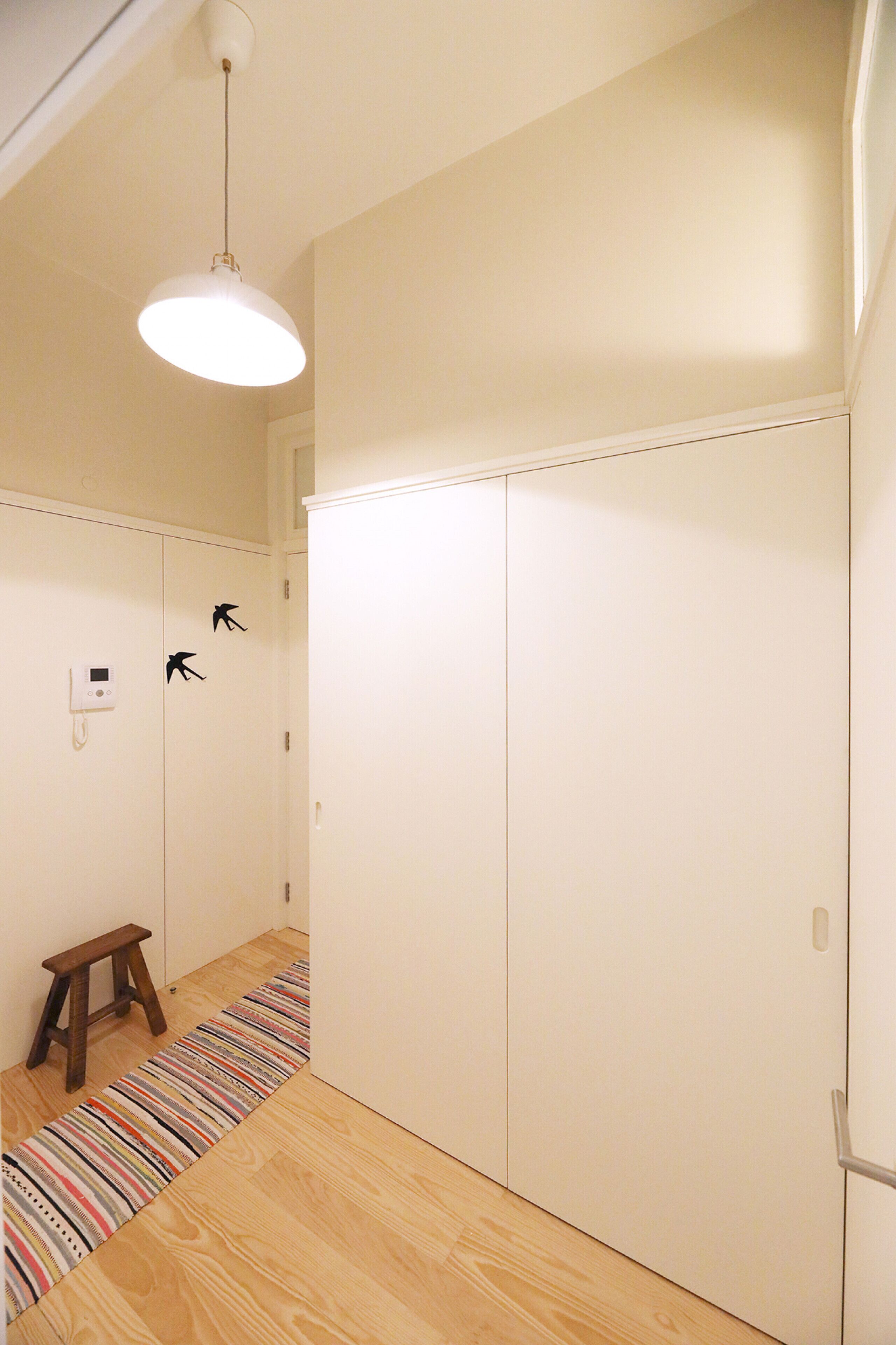 A hallway with a wooden floor, a striped rug, a small wooden stool, and a white wardrobe with a door handle.