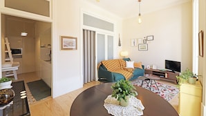 A modern living room with a sofa, TV, and dining table. - FLH Almada Cozy Apartment with View (Oporto)