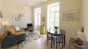 A living room with a green sofa, a dining table with chairs, a TV, and framed pictures on the wall. - FLH Almada Cozy Apartment with View (Oporto)