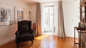 A room with wooden flooring, a black armchair, a fire extinguisher, and a door leading to a balcony. - FLH Castle Duplex with Terrace (Lisbon)