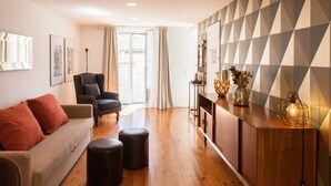 A modern living room with a sofa, ottomans, a chair, a wooden sideboard, and a geometric-patterned wall. - FLH Castle Duplex with Terrace (Lisbon)