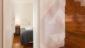 A hotel room with a wooden staircase, a bed with a grey blanket, and a bedside table with a lamp. - FLH Castle Duplex with Terrace (Lisbon)