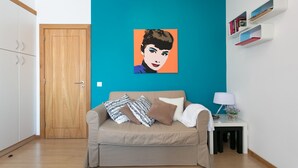 Un salón con un sofá color beige, una pared de acento color turquesa, una puerta de madera y una mesita auxiliar blanca con una lámpara y libros.