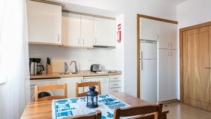 Una cocina compacta con armarios blancos, una mesa de madera con sillas, un farol y un refrigerador pequeño.