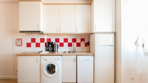 Cuina compacta amb armaris blancs, rentadora, rentavaixelles i cafetera.